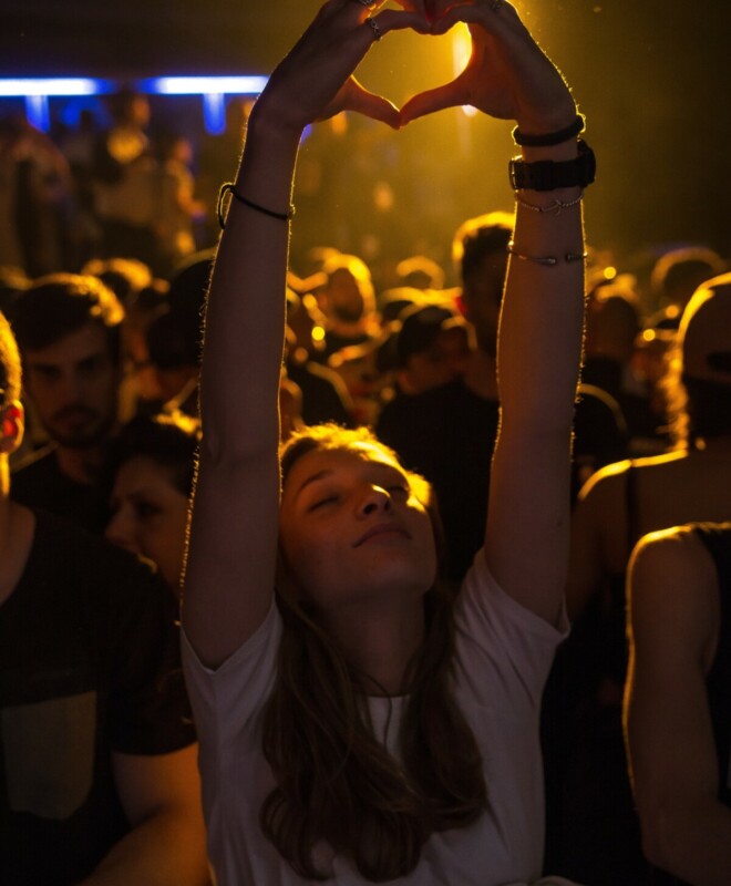 Woman at concert with eyes closed making a heart shape with her hands