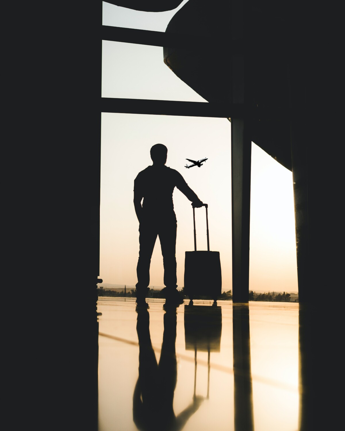 Silhouette of man standing in an airport with plane flying in background at sunset